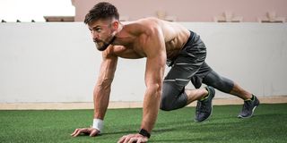 Young shirtless muscular man warming up before a workout outdoors.